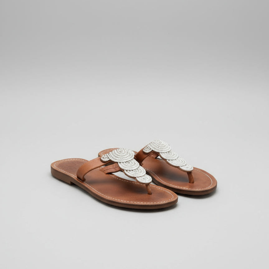 A pair of brown leather sandals with white intricate details on a wooden surface.